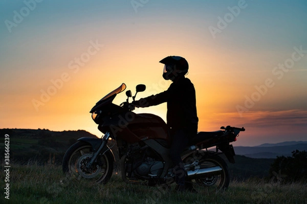 Fototapeta Man on his motorbike riding into sunset