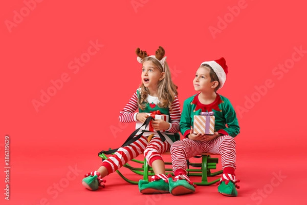 Fototapeta Cute little elves with Christmas gifts and sledge on color background