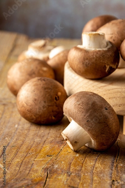 Fototapeta Top view of portobello mushrooms on wooden board and rustic table, with selective focus, dark background, in vertical with copy space