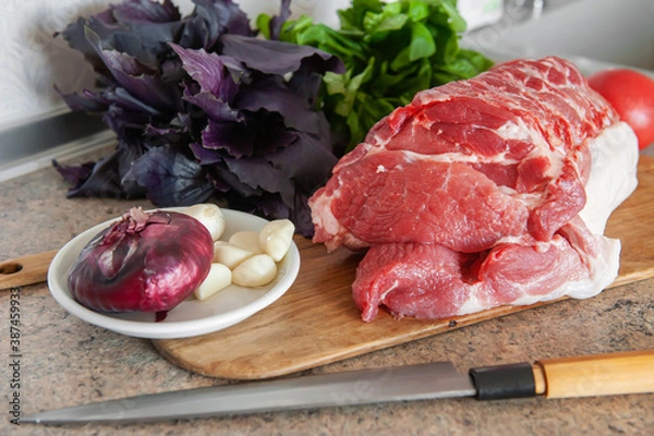 Fototapeta raw meat, a large piece of fresh pork on a chopping Board. A piece of pork with Basil, tomato and garlic is ready for cooking