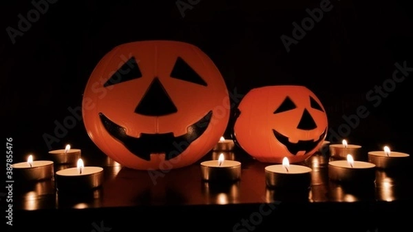 Obraz Two orange pumpkins on a table with candles around it. Scary glowing pumpkin face on Halloween night. Holiday symbol. Halloween concept.