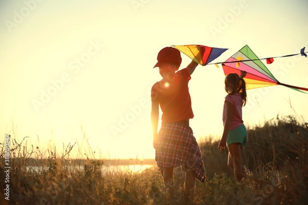 Fototapeta Little children playing with kites outdoors at sunset. Spending time in nature