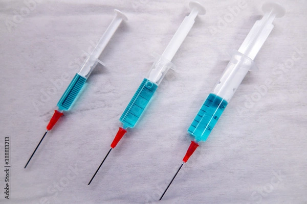 Fototapeta 3 differently sized syringes filled with blue liquid lie on a white compress