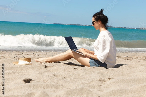 Fototapeta Young woman using laptop computer on a beach. Vacation lifestyle communication. Freelance work concept