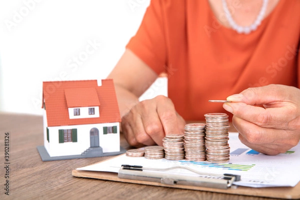 Fototapeta The East Asian old man is placing increasing dollar coins and a small house model beside him