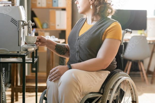 Fototapeta Young businesswoman in wheelchair making coffee at break in office environment