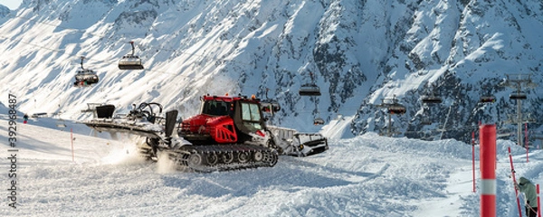 Fototapeta Red modern snowcat ratrack with snowplow snow grooming machine preparing ski slope piste hillalpine skiing winter resort Ischgl in Austria. Heavy machinery mountain equipment track vehicle. panoramic