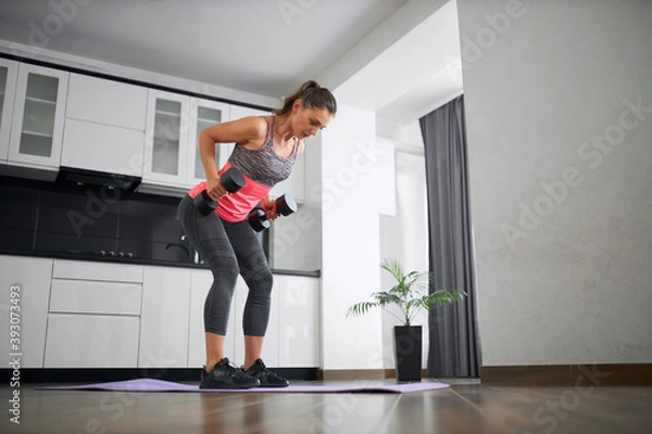 Fototapeta Fit young woman training back at home using weights.