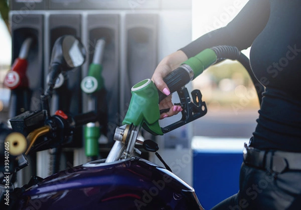 Fototapeta Female's gentle hand is holding a fueling gun. Motorcycle's tank is fueling by female owner.