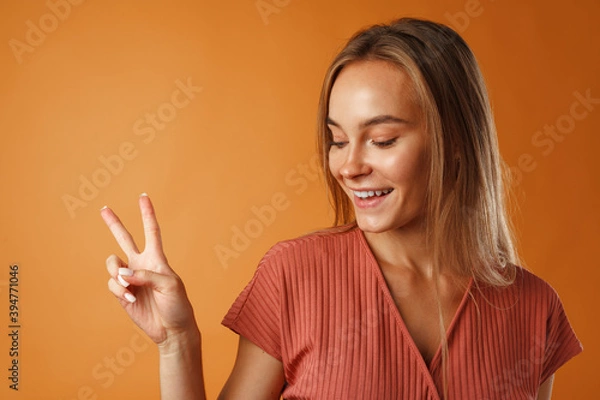 Fototapeta Young happy smiling woman showing victory sign.