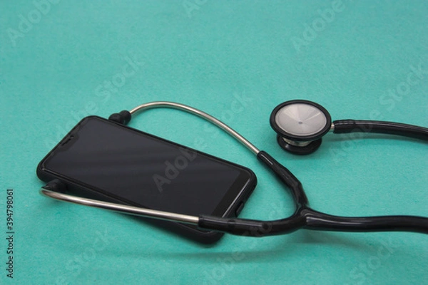 Fototapeta A smart phone surrounded by a stethoscope on green background