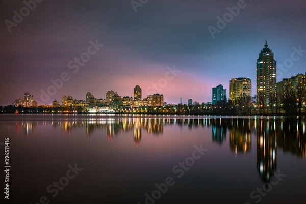 Fototapeta Night view of modern buildings in the Obolon district of Kiev, Ukraine, close to the Dnieper River, The lights reflect on the calm water.