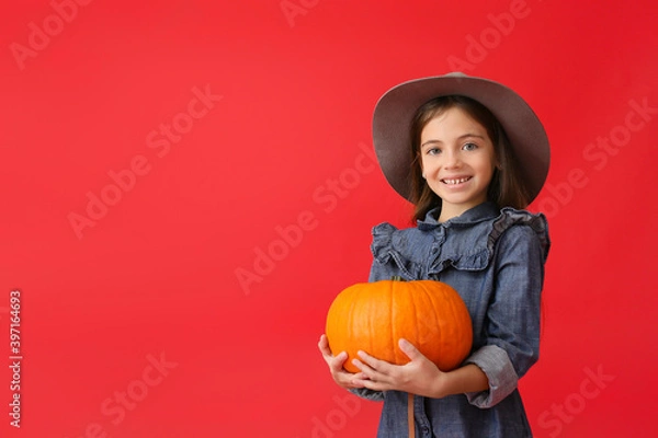 Fototapeta Cute little girl in autumn clothes and with pumpkin on color background