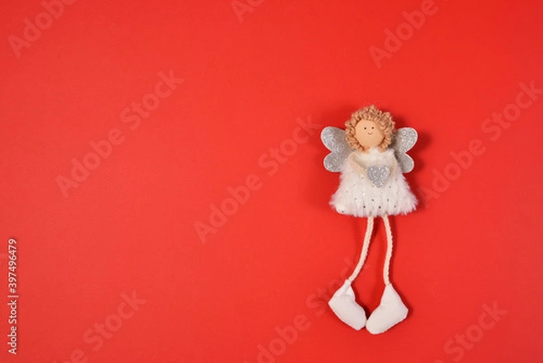 Fototapeta A white angel with silver wings, a heart in his hand and curly Golden hair lies on a red background. A beautiful angel girl holds a heart in her hands and smiles