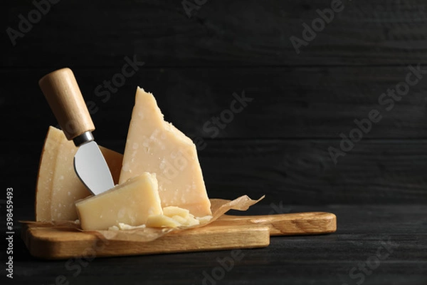 Fototapeta Pieces of Parmesan cheese and knife on black wooden table. Space for text