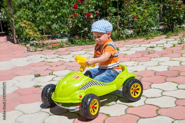 Fototapeta Happy boy drives a green children's car