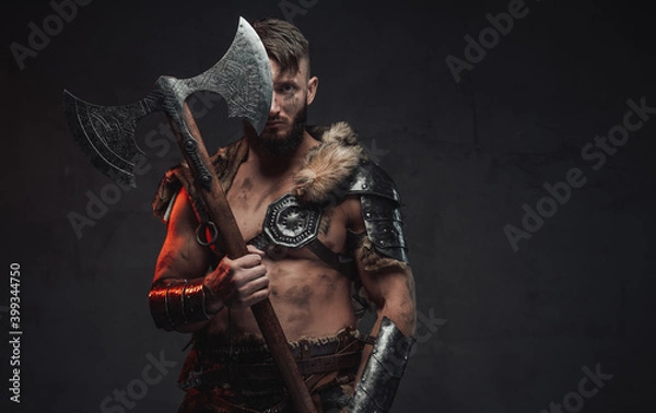 Fototapeta Armed with huge two handed axe nordic barbarian in light armour in dark background.