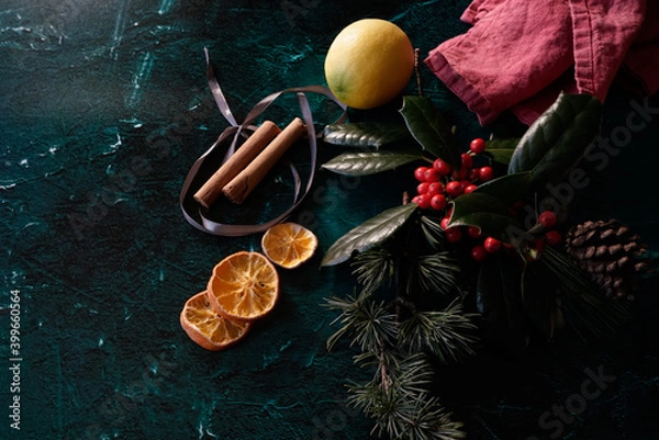 Fototapeta Arrangement of Christmas decorations: green conifer, red berries, ribbons and oranges on a dark background. 