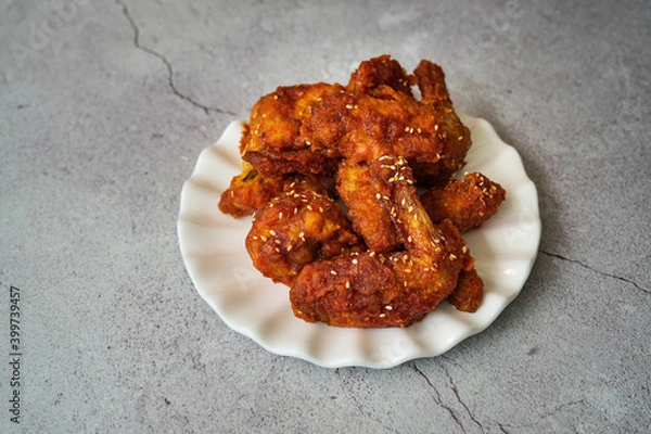 Fototapeta Deep fried chicken wings and drummets coated with hot and spicy Korean sauce on a white plate and green cloth.