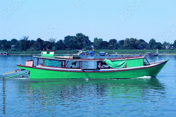 Fototapeta green wooden boat on the river with riverside and blue sky in the background