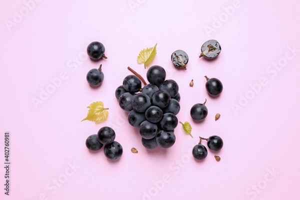 Fototapeta Bunch of ripe dark blue grapes with leaves on pink background, flat lay