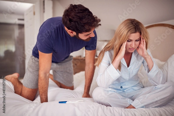 Fototapeta Disappointed Couple Wearing Pyjamas In Bedroom Holding Pregnancy Test