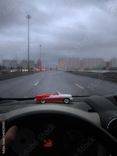 Fototapeta Toy car vintage convertible Pontiac 1950th on the front dashboard of the car. Gray, gloomy, rainy winter weather outside. California dreaming.