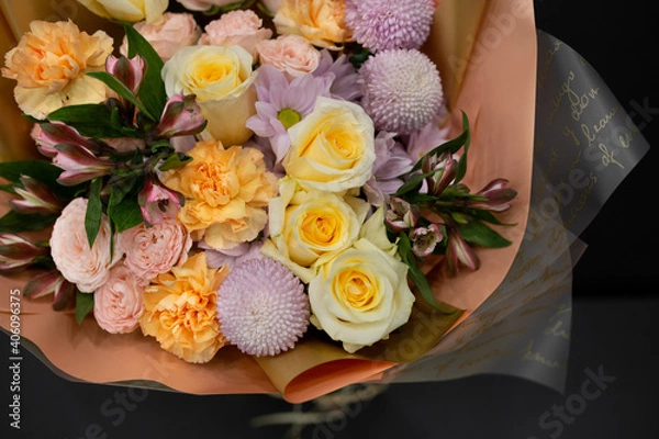 Fototapeta A bouquet of flowers with yellow roses and other flowers in decorative packaging on a dark background.