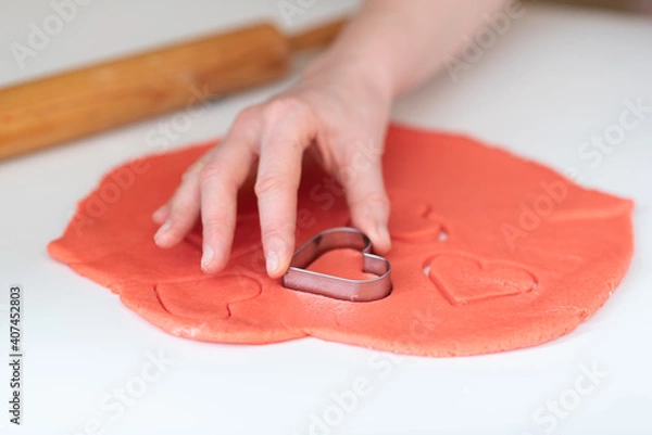 Fototapeta A woman makes homemade Valentine's Day cookies from shortcrust pastry in the form of red hearts.