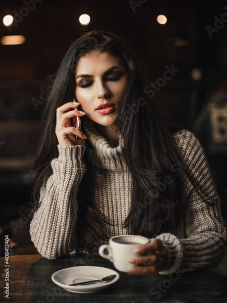 Fototapeta Woman talking on phone and drinking coffee in a cafe.