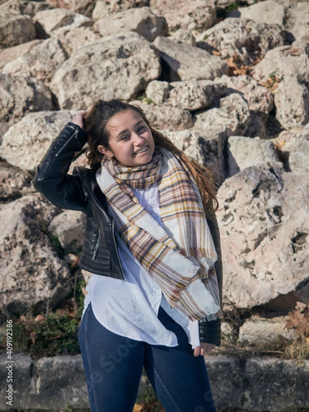 Fototapeta Vertical shot of a young caucasian female posing against the stone wall