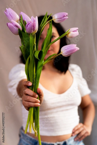 Fototapeta young woman holding lilac tulips with natural soft light and casual informal dress. concept of spring time and femininity. authentic people, natural looking portrait and lifestyle