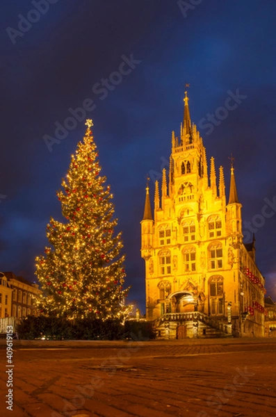 Fototapeta Gouda, The Netherlands, December 30, 2020 the market square in the holiday season, with a large Christmas tree next to the illuminated historic town hall