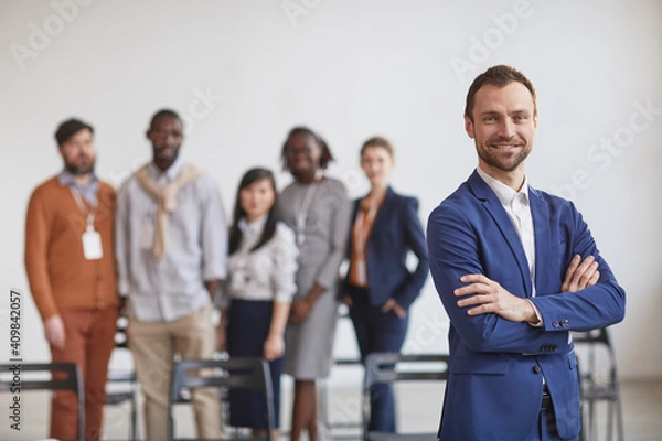 Fototapeta Waist up portrait of successful businessman standing with arms crossed against multi-ethnic team in background, copy space