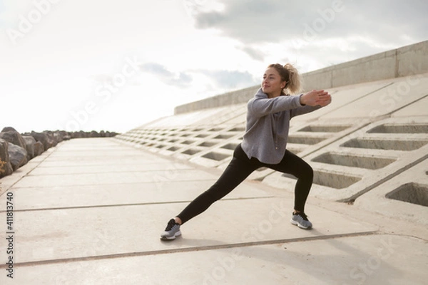 Fototapeta Attractive sporty woman in sportswear trains outdoors. Warm up or stretching, healthy lifestyle.