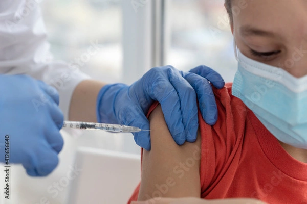 Fototapeta boy in medical mask during vaccination process, doctor is making injection.  Boy is not scared and wait doctor to finish. Vaccination concept.