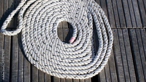 Fototapeta strong white nautical rope in a circle around a pier on the background of wooden boards