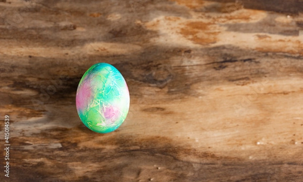 Fototapeta Multicolored marble Easter egg on a wooden textured background. Horizontal orientation. Top view.