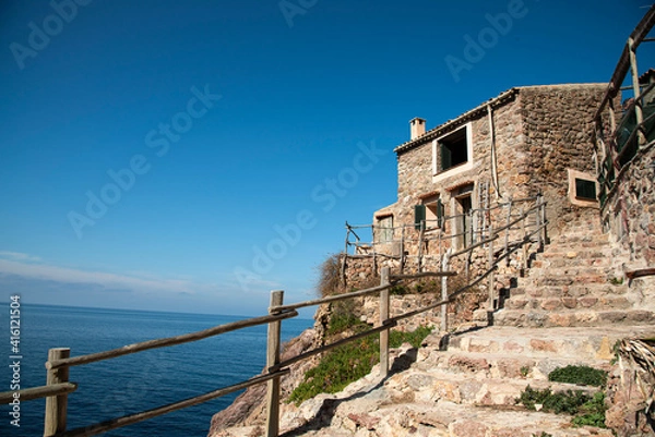 Fototapeta Mallorcan house by the sea. The rocky walls and the green shutters of Majorca carriages. House by the sea, in a small pub in the Sierra de Tamuntana area.