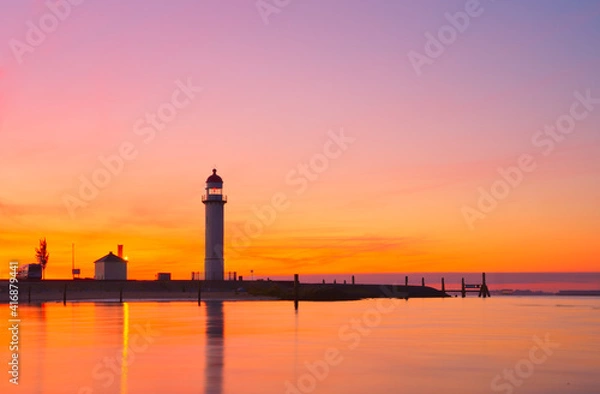 Fototapeta Silhouette of a lighthouse by the sea under orange sunset sky