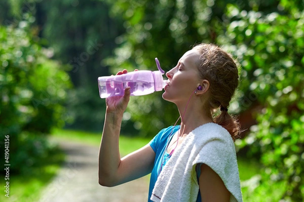 Fototapeta Fitness woman drinking water after running training in summer park