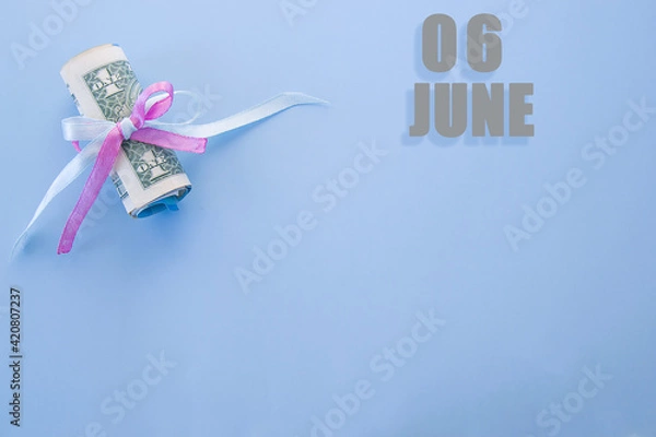 Fototapeta calendar date on blue background with rolled up dollar bills pinned by blue and pink ribbon with copy space. June 6 is the sixth day of the month