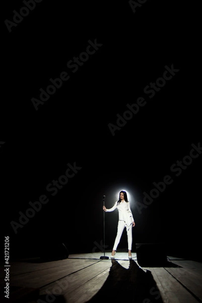 Fototapeta Singer woman on stage with black background in a beam of white light.