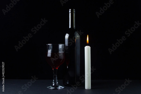 Fototapeta Wine and candle on a dark background. Creative photo of red wine on a black background. Wine by candlelight