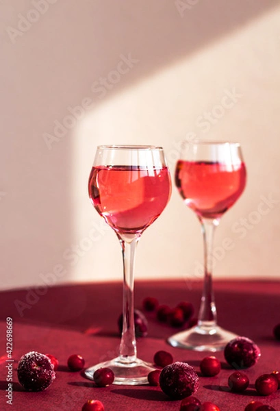 Fototapeta two glasses with pink gin infused with cranberry, light and shadow on the background, berry liqueur or red alcoholic cocktail