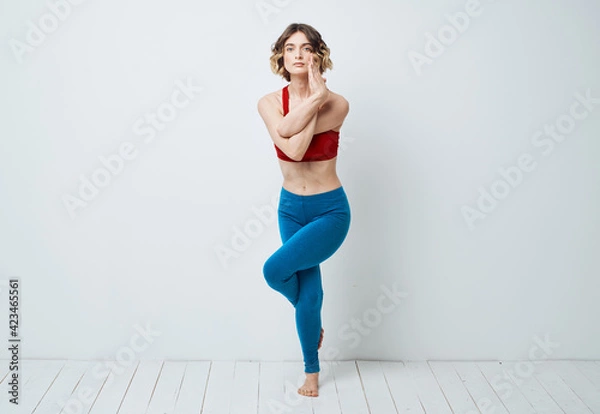 Fototapeta A woman in blue leggings does exercises on a light background of yoga asana