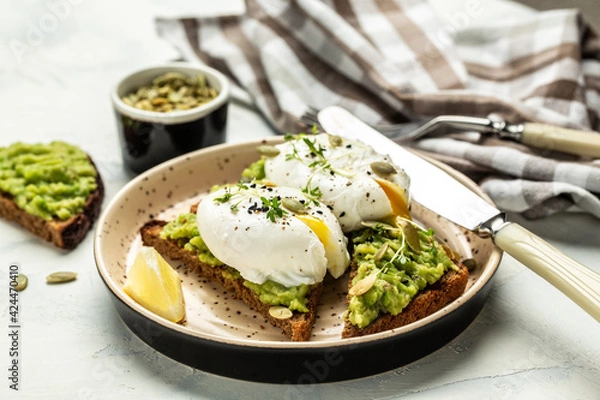 Fototapeta Avocado Sandwich with Poached Egg and avocado on toasted bread. Delicious breakfast or snack on a light background, top view