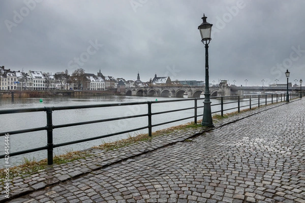 Fototapeta Maastricht, Netherland 04-07-2021 Downtown view on the city of Maastricht during an unusual snow fall in April. Snowflakes are still falling down giving nice reflections on the cobblestone streets