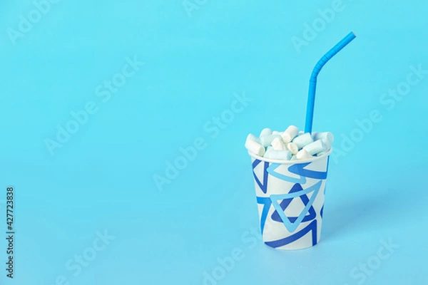 Obraz Paper cup with blue and white marshmallows with a Drinking straw, blue background