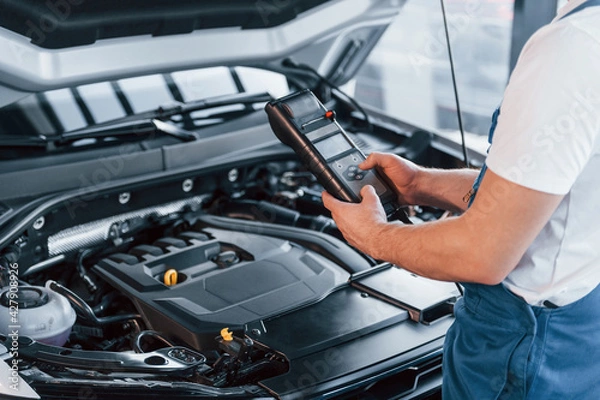 Fototapeta Young man in white shirt and blue uniform repairs automobile